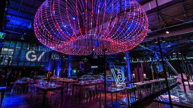 Indoor evening event with tables and a chandelier made of multiple lit rings.