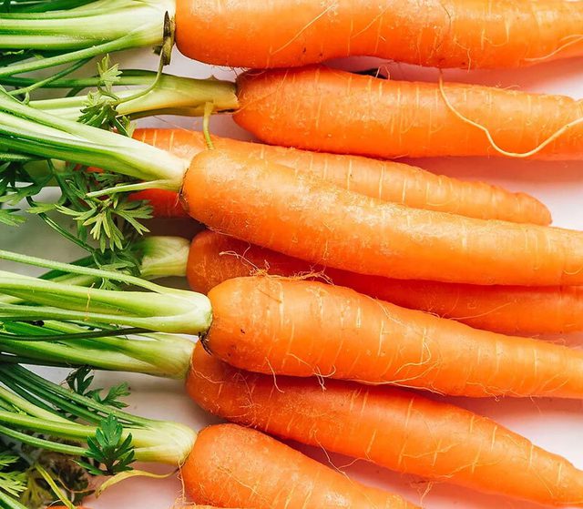 Carrot sticks with green leafy tops in a row.