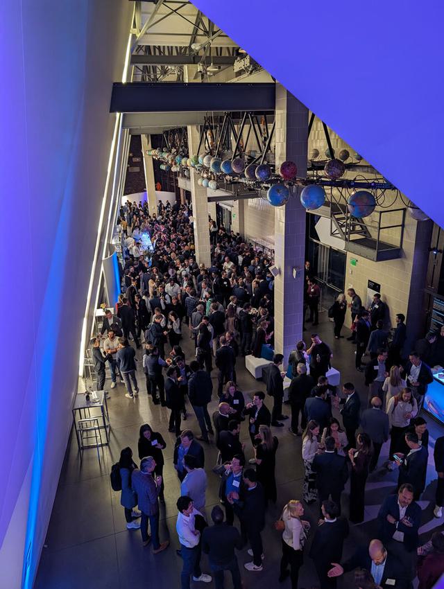 Crowd of people at an event with purple lighting and globe chandeliers.