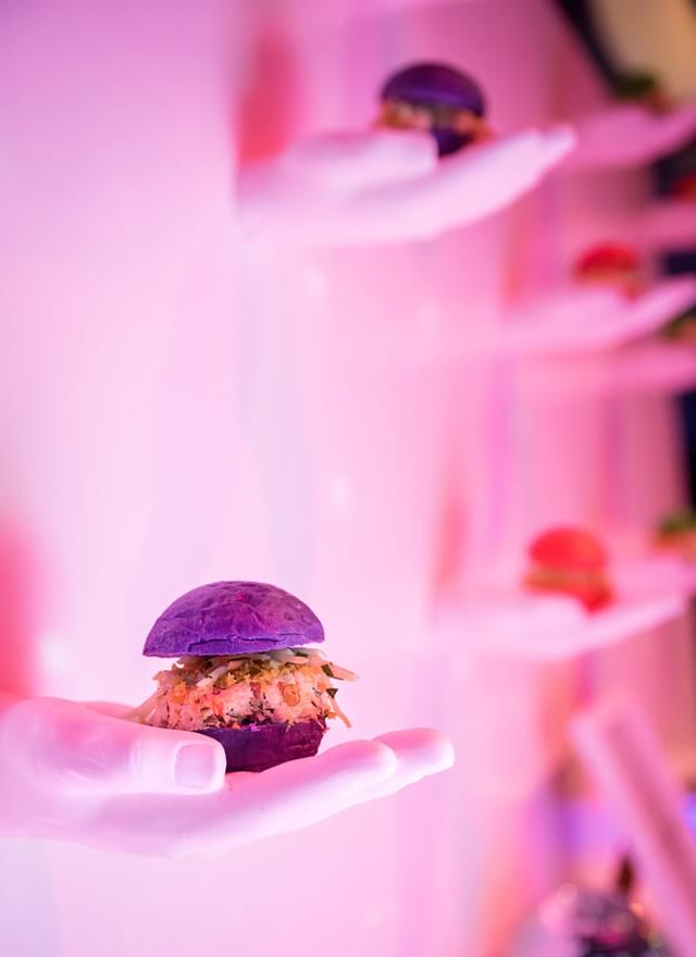Pink wall with purple bun sliders resting on shelves that look like hands.