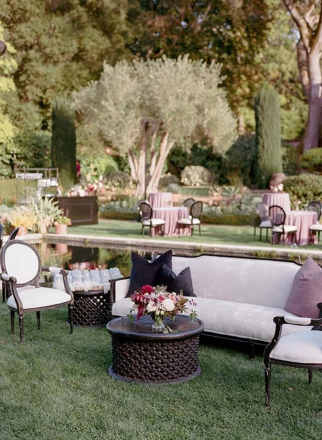 Outdoor seating area with black and white benches and chairs in a lush green garden setting.